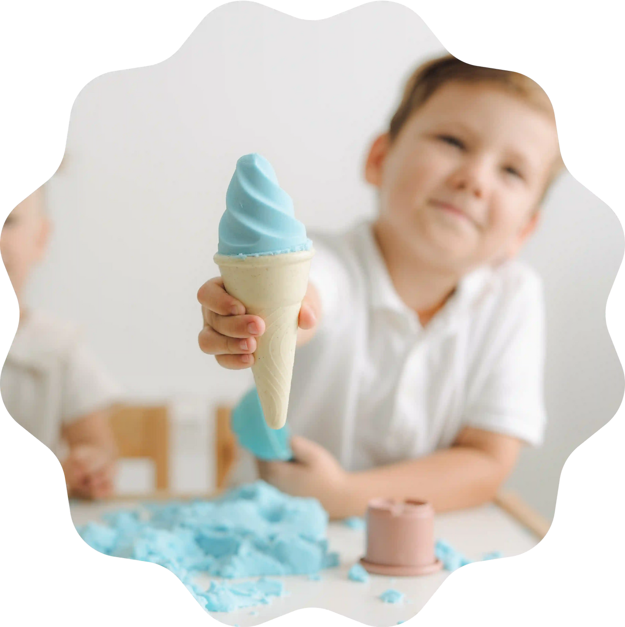 Ein Junge hält stolz ein blaues Eis aus Sandolin Zaubersand in der Hand, geformt mit Förmchen am Tisch.