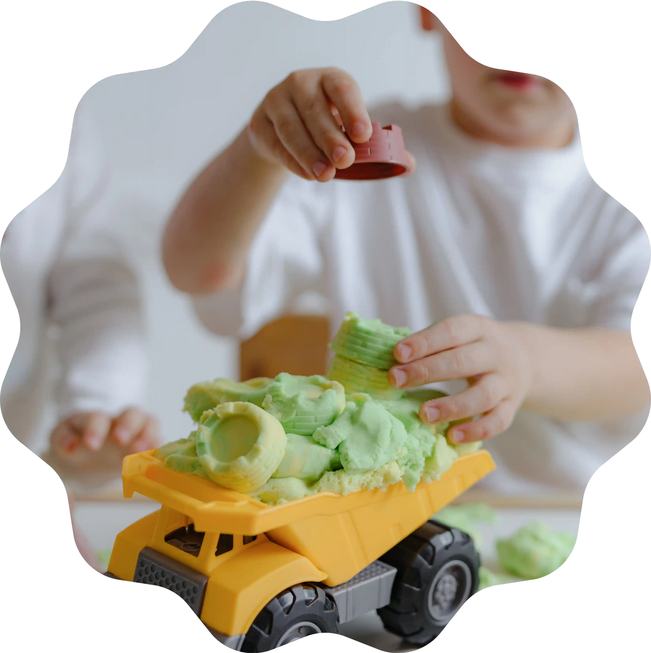 Kinderhände beladen einen gelben Spielzeug-LKW mit grünem Sandolin Zaubersand und kleinen Förmchen.