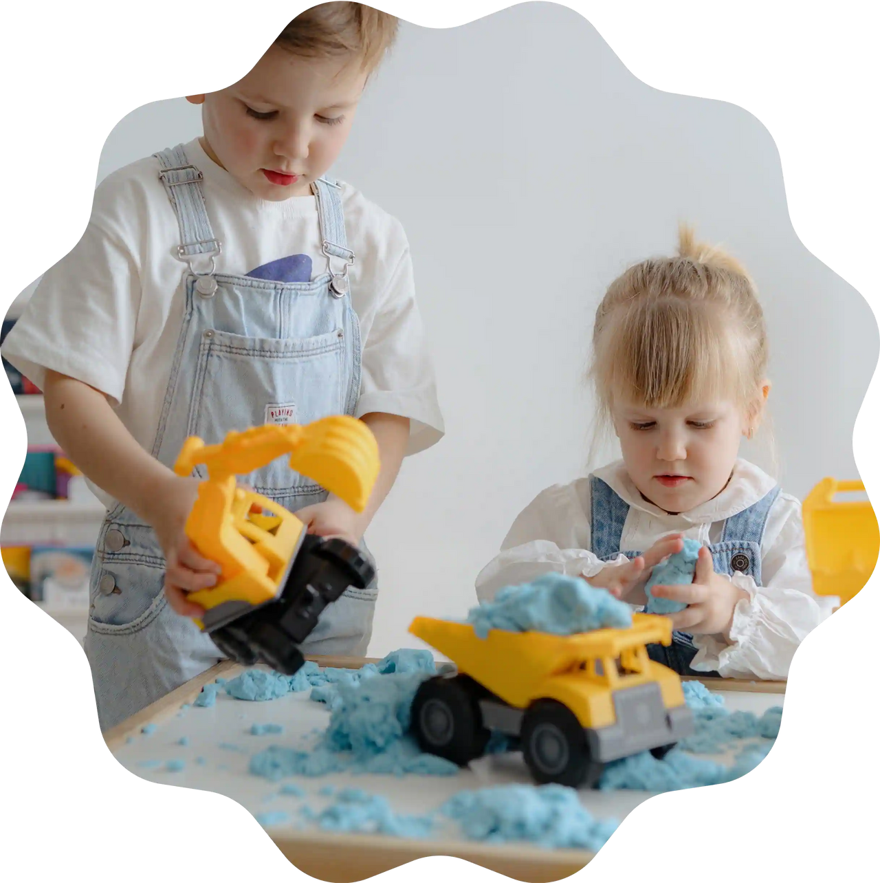 Zwei Kinder spielen mit einem gelben Spielzeug-Bagger und einem LKW, die mit blauem Sandolin Zaubersand beladen sind.