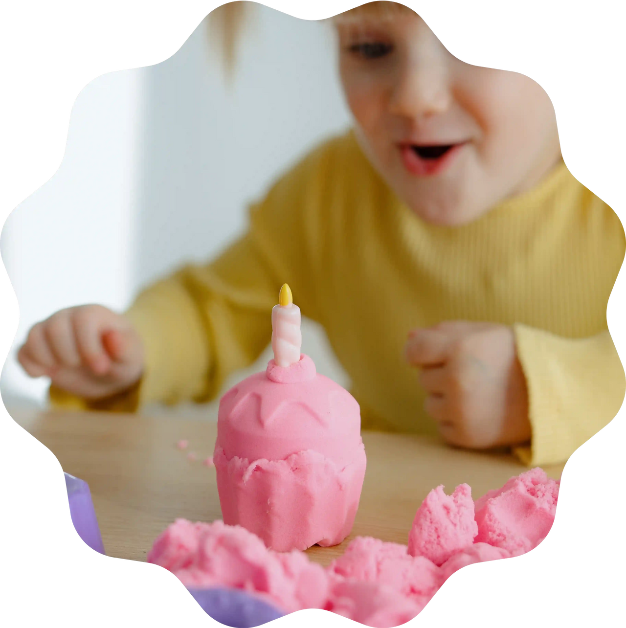 Ein Mädchen freut sich über einen pinken Cupcake aus Sandolin Zaubersand mit Kerze, geformt am Tisch.